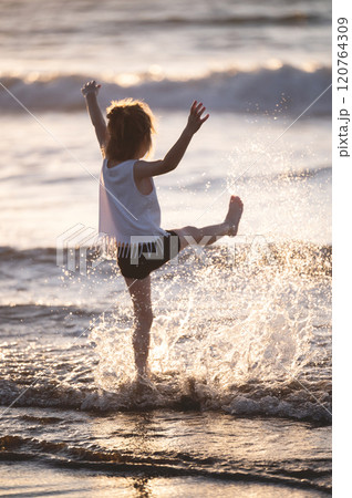 Child plays joyfully in ocean waves at sunset on warm summer evening Child plays joyfully in ocean waves at sunset on warm summer evening 120764309