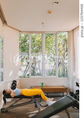 Woman in Blue Yellow outfit does Dumbbell Bench Press for chest workout. 120764488