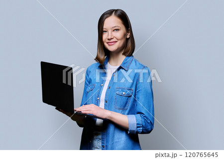 Smiling young woman with laptop on grey studio background 120765645