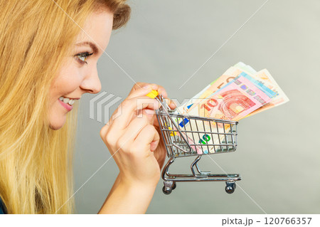 Happy woman holding shopping cart with money Happy woman holding shopping cart with money 120766357