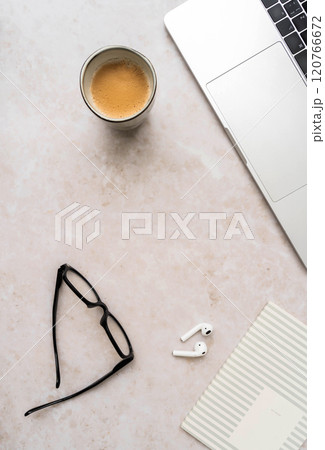 Minimal workspace with laptop, black glasses, coffee cup, wireless earbuds, and striped notebook on white desk Minimal workspace with laptop, black glasses, coffee cup, wireless earbuds, and striped notebook on white desk 120766672