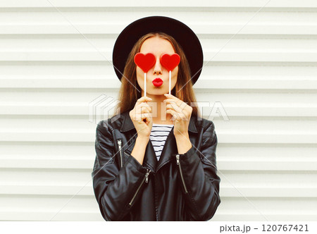 Fashion portrait sweet woman with red lipstick blowing kiss with lollipop heart in black hat, jacket 120767421