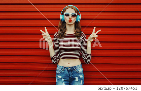 Portrait of happy young woman with wireless headphones listening to music on a red background Portrait of happy young woman with wireless headphones listening to music on a red background 120767453