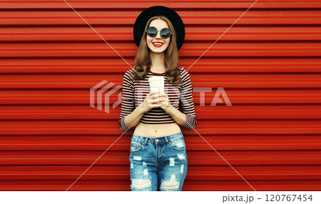 Portrait of happy young woman with cup of coffee wearing a black round hat on a red background 120767454
