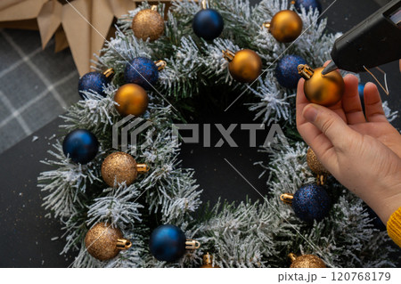 Crafter using hot glue Handmade Christmas wreath from festive blue and yellow decorations. Festive holiday preparation craft master class of creative making decor. Hands-on activities sustainable 120768179
