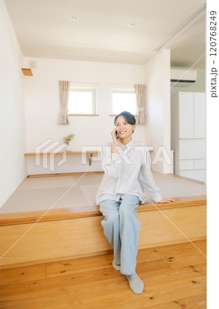 畳の小上がりに座り電話をする女性 120768249