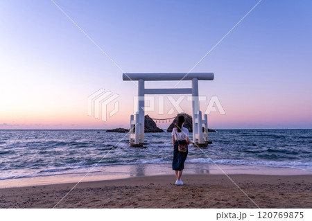 福岡県糸島市　夕方の桜井二見ヶ浦の夫婦岩と白い鳥居の前でポーズをとる女性 120769875