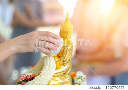 Songkran festival, Thai New Year. female hand holding silver bowl pouring water with jasmine and roses onto buddha statue. 120770673