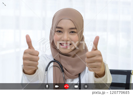 young muslim female medical doctor with stethoscope showing thumbs up sign talking to facetime video calling with smartphone  in clinic. Using videochat online app with mic, video, phone, share 120770685