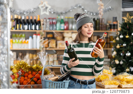 Young woman examines alcohol whisky bottle in store. Young woman examines alcohol whisky bottle in store. 120770873
