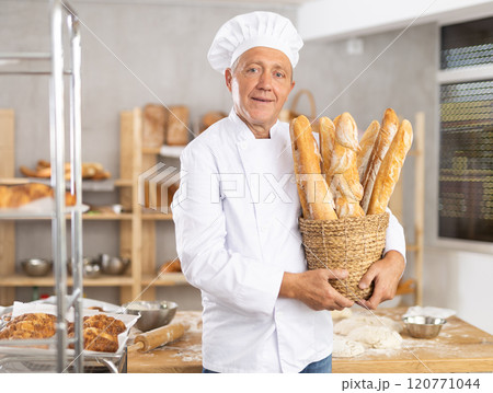 Bakery mature man employee holds basket of ready-made baguettes. 120771044
