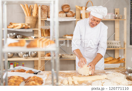 Senior man works in bakery as baker, kneads dough, works with flour. 120771110