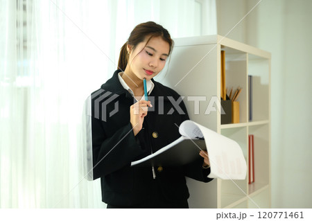 Young businesswoman in a black coat thoughtfully examining a report near bookshelf 120771461