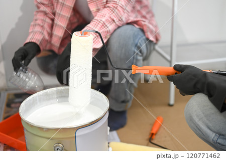 Close up of painter dipping a handled roller into a bucket of white paint for wall application Close up of painter dipping a handled roller into a bucket of white paint for wall application 120771462
