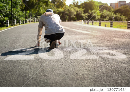 Runner crouching in a starting position on road with the numbers 2025. New beginning and goal concept Runner crouching in a starting position on road with the numbers 2025. New beginning and goal concept 120771484