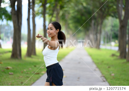 Young woman in sportswear warming up her body preparing for workout in serene park 120771574