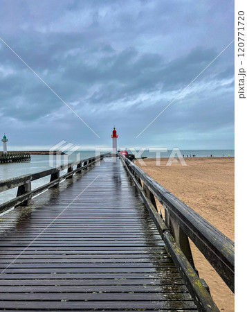 Red lighthouse with wooden pier with blue sky with rainy clouds background in the Normandy, France.  120771720