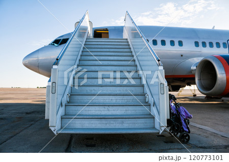 Airplane with a passenger boarding steps on the airport apron with a stroller prepared for the carriage of children 120773101