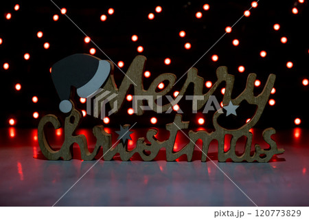 Merry Christmas wooden message on dark bokeh light garland background. New year and Christmas preparation. Handmade eco-friendly decor. Sustainable Merry Christmas wooden message on dark bokeh light garland background. New year and Christmas preparation. Handmade eco-friendly decor. Sustainable 120773829