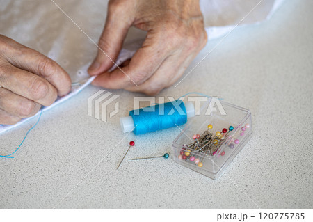 Re-stitching old things. Elderly female hands in the process of sewing, threads and pins in the foreground in focus, close-up, selective focus. Re-stitching old things. Elderly female hands in the process of sewing, threads and pins in the foreground in focus, close-up, selective focus. 120775785