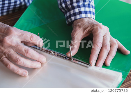 Senior female hands with opened green plastic file folder, person closing the clip, close-up, selective focus. Senior female hands with opened green plastic file folder, person closing the clip, close-up, selective focus. 120775786