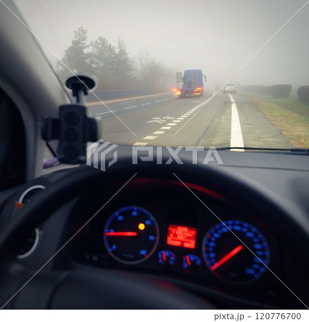 Car traveling on the foggy road with headlights or headlamps on. Low visibility - Dangerous driving of cars in winter in bad weather. 120776700
