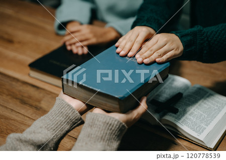 Group of Christians sit together and pray around a wooden table with blurred open Bible pages in their homeroom. Prayer for brothers, faith, hope, a Group of Christians sit together and pray around a wooden table with blurred open Bible pages in their homeroom. Prayer for brothers, faith, hope, a 120778539