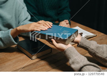 Group of Christians sit together and pray around a wooden table with blurred open Bible pages in their homeroom. Prayer for brothers, faith, hope, a Group of Christians sit together and pray around a wooden table with blurred open Bible pages in their homeroom. Prayer for brothers, faith, hope, a 120778540