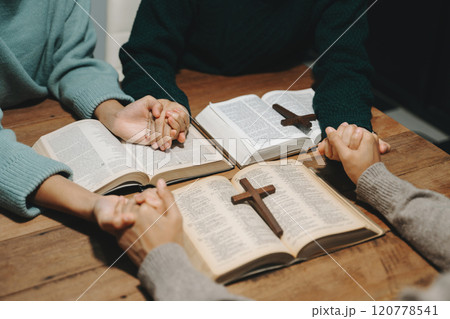 Group of Christians sit together and pray around a wooden table with blurred open Bible pages in their homeroom. Prayer for brothers, faith, hope, a Group of Christians sit together and pray around a wooden table with blurred open Bible pages in their homeroom. Prayer for brothers, faith, hope, a 120778541