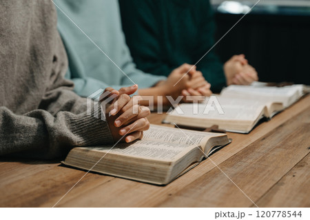 Group of Christians sit together and pray around a wooden table with blurred open Bible pages in their homeroom. Prayer for brothers, faith, hope, a Group of Christians sit together and pray around a wooden table with blurred open Bible pages in their homeroom. Prayer for brothers, faith, hope, a 120778544