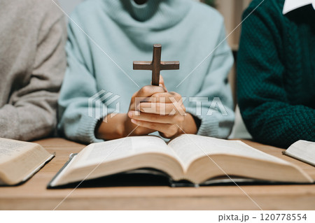 Group of Christians sit together and pray around a wooden table with blurred open Bible pages in their homeroom. Prayer for brothers, faith, hope, 120778554