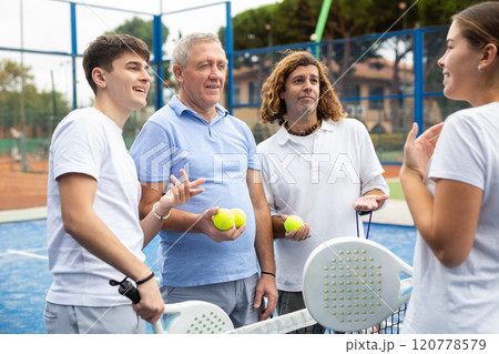 Two pairs with rackets in their hands chatting after playing padel on tennis court 120778579