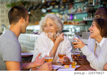 Cheerful family celebrating meeting or acquaintance with beer in bar. Focus on elderly woman 120778627
