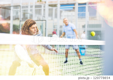 Portrait of middle-aged Latin male in sportswear enjoying popular sport padel game on tennis court outside Portrait of middle-aged Latin male in sportswear enjoying popular sport padel game on tennis court outside 120778654
