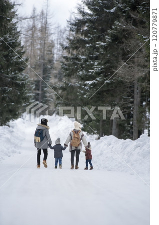 Rear view of family is enjoying winter holiday in the mountains, holding hands while walking through the snowy forest. Rear view of family is enjoying winter holiday in the mountains, holding hands while walking through the snowy forest. 120779871