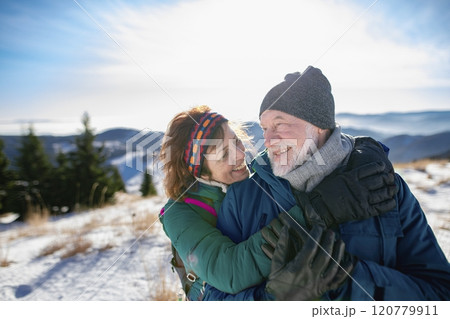 Portrait of active seniors enjoying nature. Romantic winter hike for an elderly couple in snowy mountains. 120779911