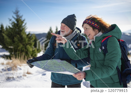Older tourist using map during their hike in snowy winter mountains. Elderly couple in winter nature. 120779915