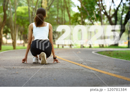 Chasing Goals in 2025. Young woman crouching in a starting position on paved path with the number 2025 120781384