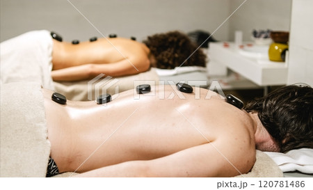Clients relaxing with hot stones on backs during massage therapy session 120781486