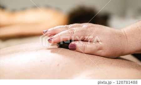 Massage therapist placing hot stone on client's back during spa treatment 120781488