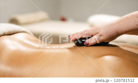 Masseur applying hot stone on woman's back during massage therapy session Masseur applying hot stone on woman's back during massage therapy session 120781512