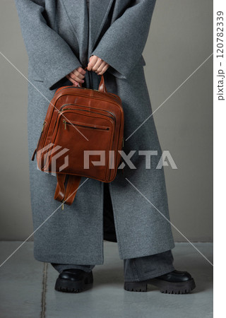 woman posing with a leather backpack wearing a warm gray coat and black boots 120782339