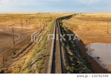 Expansive railway track winding through the arid landscape of Kazakhstan during sunset Expansive railway track winding through the arid landscape of Kazakhstan during sunset 120782599