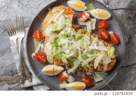 Delicious fresh schnitzel caesar salad with chicken meat, eggs, parmesan, iceberg lettuce and tomatoes close-up in a plate. Horizontal top view Delicious fresh schnitzel caesar salad with chicken meat, eggs, parmesan, iceberg lettuce and tomatoes close-up in a plate. Horizontal top view 120782650