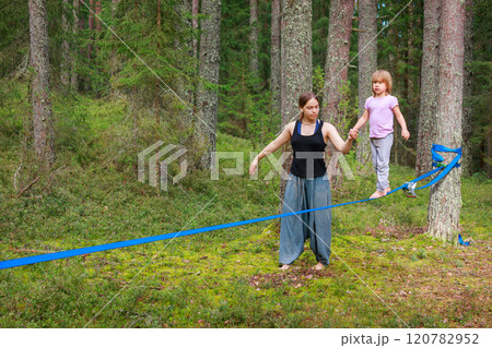 Teenage girl helping a her sister balance on a slackline in the forest Teenage girl helping a her sister balance on a slackline in the forest 120782952