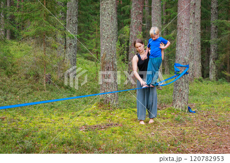 Teenage girl helping a young boy balance on a slackline in the forest 120782953