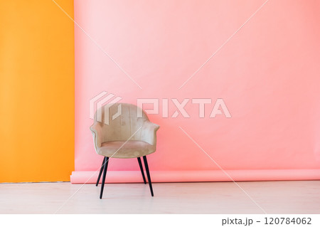 Beige chair by pink orange wall and white floor 120784062