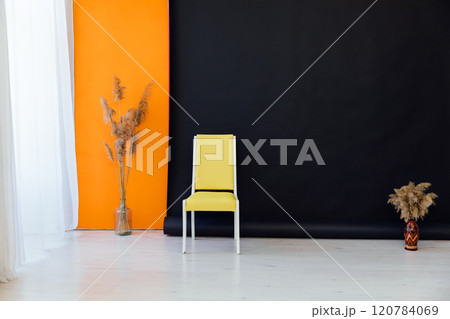 Yellow chair and dried flowers in the interior of a black and orange room 120784069