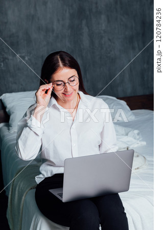Woman in glasses working online with laptop on bed Woman in glasses working online with laptop on bed 120784236