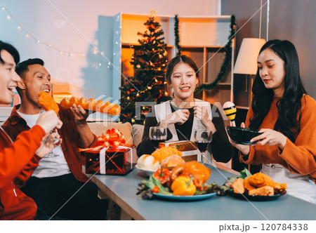 Group of young Asian man and women as friends having fun at a New Year's celebration, holding gift boxes standing by Christmas tree decoration, midnight countdown Party at home with holiday season. Group of young Asian man and women as friends having fun at a New Year's celebration, holding gift boxes standing by Christmas tree decoration, midnight countdown Party at home with holiday season. 120784338